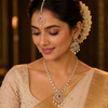 A woman wearing an ornate Indian bridal jewelry set, including a maang tikka, earrings, and necklace with lab grown diamonds and red gemstone accents, paired with a beige and gold saree.
