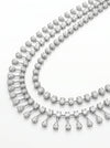 The design showcases a classic tennis-style necklace combined with pear-shaped diamond
